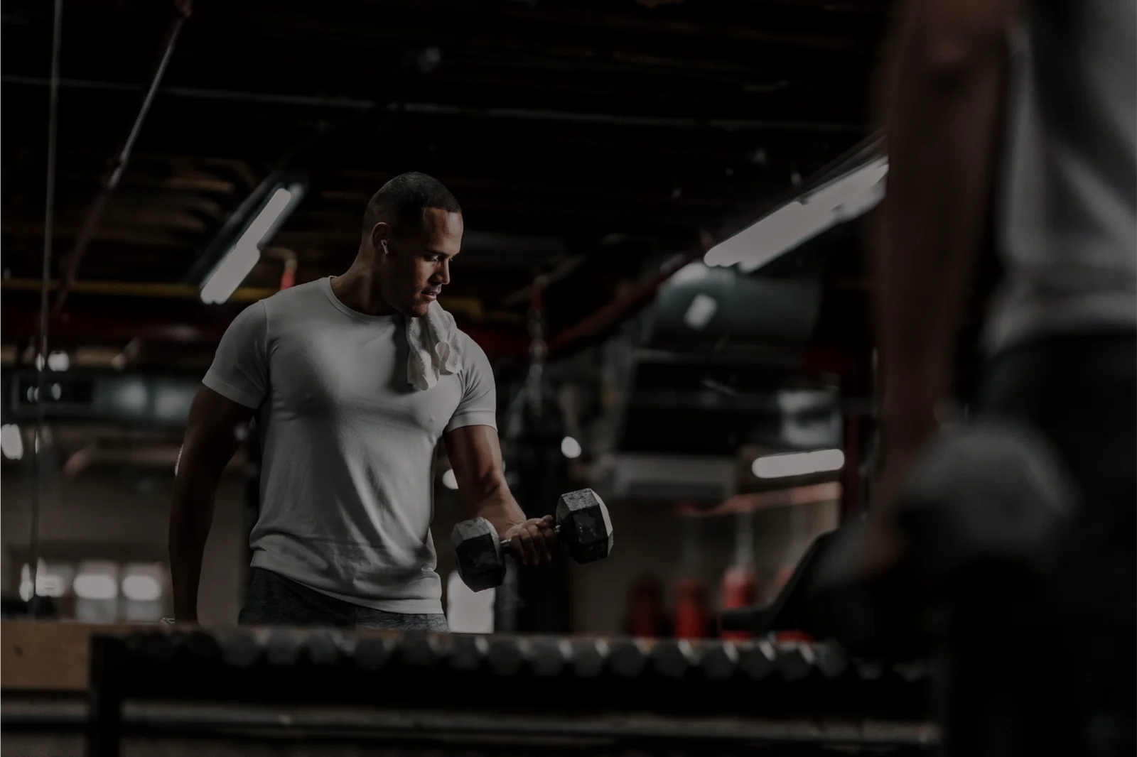 Athlete performing a dumbbell curl in a dark, professional gym